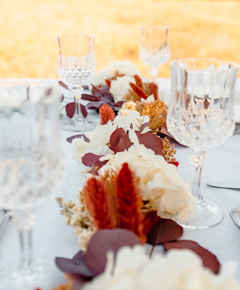 Chemin de table en fleurs séchées rosa cadaqués dans des tons rouge, orange et blanc disposé sur une table