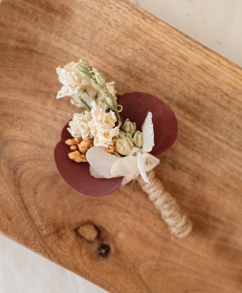 Boutonnière en fleurs séchées Rosa Cadaqués posée sur une table en bois